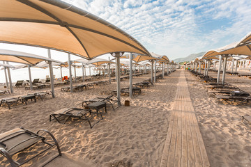 Rows of sun loungers on a sandy beach with sun shades. Relaxation and luxury beach holidays