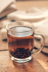 A cup with black brewed tea on a wooden table with book and a warm sweater. Concept cozy autumn or winter vacation.