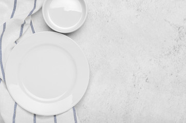 Clean white plates on fresh towel with stripes on a stone light minimalist background. Top view, copy space, flat lay.