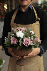 Naklejka premium Festive flower arrangement of paleviolet roses and cotton flowers in the vase florist holding at the flowers boutique.