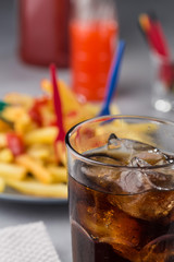 fizzy drink with ice in a glass on the background of a plate with fried potatoes