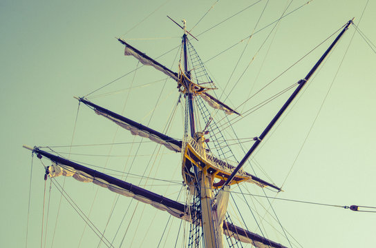Mast of a sailing ship, with raised sails against the clear sky.