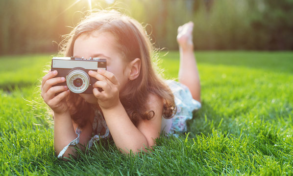 Cute little girl lying on green lawn and taking a picture