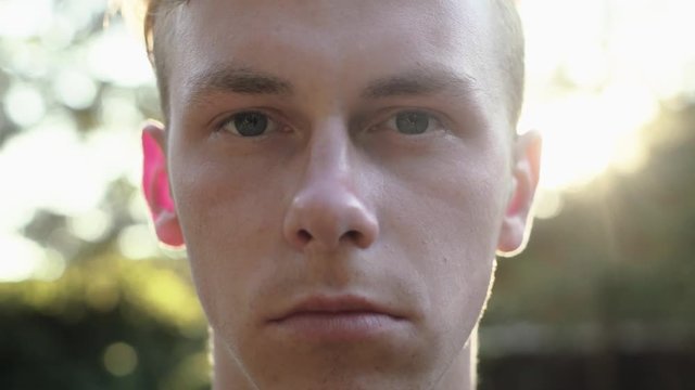 Young serious upset guy looking directly into camera with sun in the background