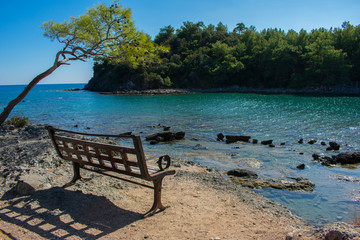 Fototapeta na wymiar empty bench on coast of sea. beautiful landscape, sunny day on phaselis beach in antalya, turkey 