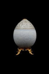 Easter egg from porcelain on a bronze stand on a black background.