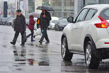 Few pedestrians on a pedestrian crosswalk in front of the car. Rainy weather.