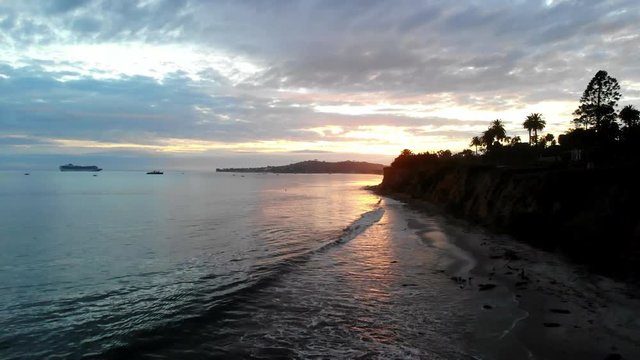 Aerial drone shot at sunset overlooking the Pacific Ocean and California cliffs of Santa Barbara from Butterfly Beach in Montecito.