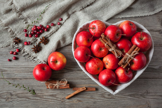 Red cinnamon apples in a heart shape basket and cranberries on wooden background