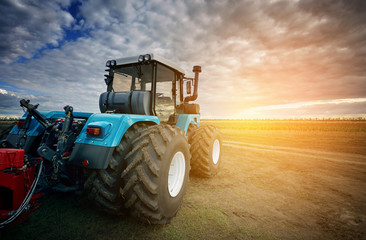 Fototapeta premium Tractor working in the field in the background of the sunset