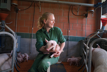 Spass am Beruf, junge Landwirtin im Stall mit Ferkel im Arm