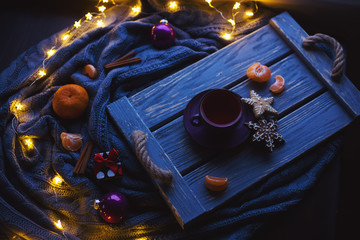 Fruit tea and Christmas homemade cookies on wooden tray surrounded by New Year decorations with citrus and warm garland lights