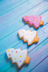 Closeup three homemade glazed gingerbread made in form of Christmas tree on blue wooden background