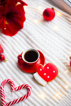 Red cup with espresso coffee and gingerbread in form of glove on white knitted plaid surrounded with winter decor.