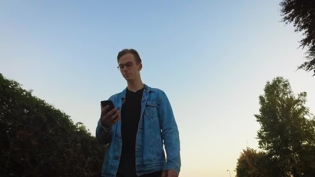 Young guy walking on the street looking into his phone swiping tinder