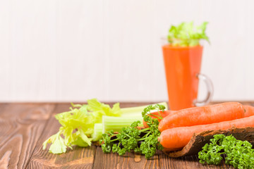 Carrot and celery juice with fresh vegetables on bark plates on wooden background.