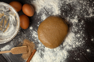The process of preparing dough for Christmas cookies with cinnamon, ginger and sugar. On a dark brown background sprinkle with flour. Ingredients for cookies. New year's magic. With the blur