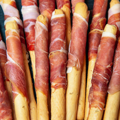 Appetizing grissini with ham. Closeup view square photo.