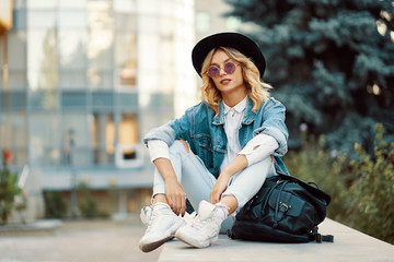 Stylish girl spent time in the city sitting near modern glass bu