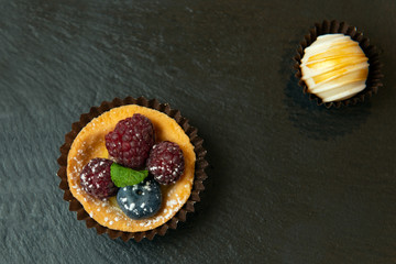 Beautiful desserts with raspberries an blueberry on black matte surface. Closeup view.