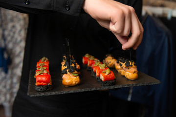 Hand in black shirt takes snack with salmon from black tray. Catering.