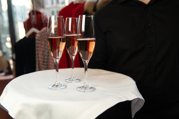 Waiter holding tray with rose champagne in wine glasses.