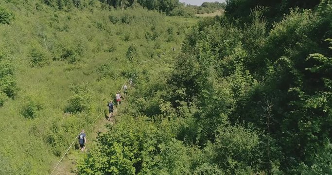 Aerial shot of people running a competition on a trail in a small valley through the woods during summer.