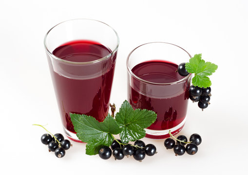 Black currant juice in glasses and ripe berries on a white background.