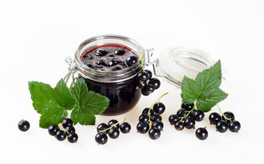 Black currant jam in a jar and ripe berries on a white background.