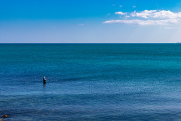 a fisherman fishing in the sea, in the city of Trani, with the Monastery of Santa Maria di Colonna in the background. In Puglia, near Bari, in the province of Barletta, Andria, Trani. Sea and blue sky