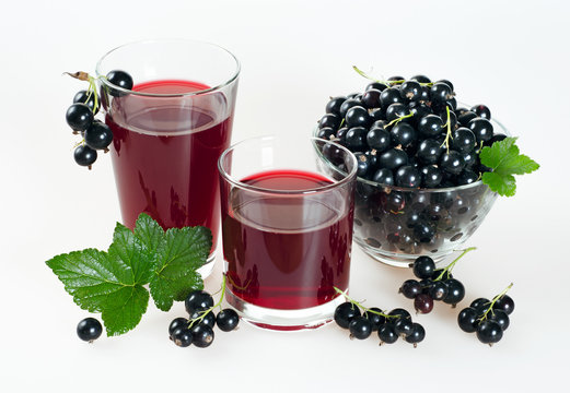 Black currant juice in glasses and ripe berries on a white background.