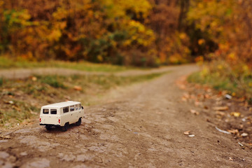 miniature toy car minivan rides on the road on the background of yellow autumn trees. The concept of travel. Copy space