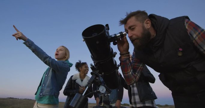 Group of adult multiracial friends looking through telescope together spending time in nature