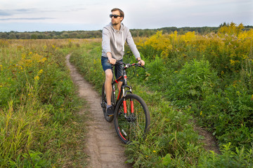 Naklejka premium Young men on bike in field with flowers, beautiful landscape