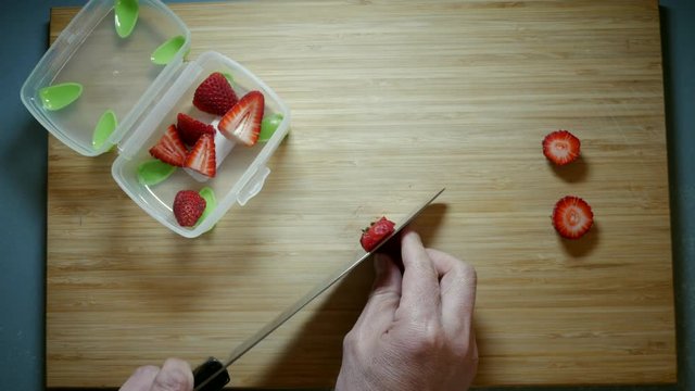 Strawberries being sliced on a bamboo chopping board. Fruit being prepared for children&sbquo;&Auml;&ocirc;s lunch. Top down angle.