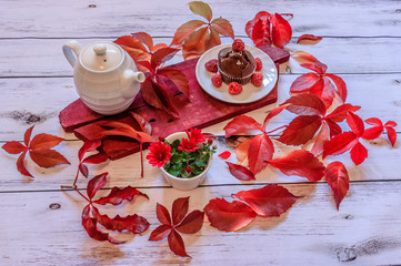 Autumn composition.Red leaves, teapot and muffin with raspberries on wooden background