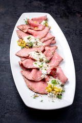 Traditionelles bayrisches Brotzeit Gericht mit kaltem Rostbraten aufgeschnitten mit Remoulade als closeup auf einem weißen Teller 