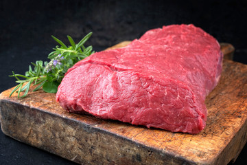 Raw roast beef with herbs offered as closeup on an old rustic wooden cutting board