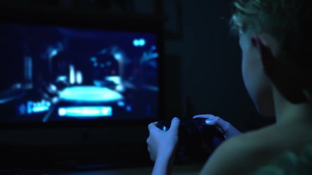 4K footage of a Young teenager Boy using the gamepad plays a computer  Online Video Game at night. 