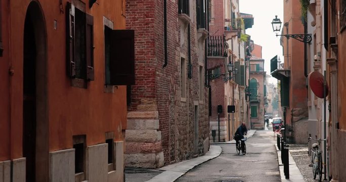 An old and alone man while cycling in a narrow street in the city of Verona, Italy.