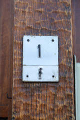 House number one F 1F in pressed metal black digits on white background and attached to wooden house wall in Belgium
