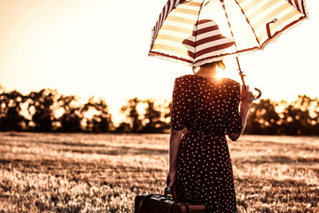 photo of the beautiful young woman with red umbrella and brown suitcase standing in the field