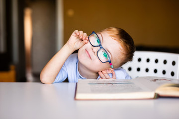 Cute toddler boy with down syndrome with big glasses reading intesting book