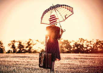 photo of the beautiful young woman with red umbrella and brown suitcase standing in the field