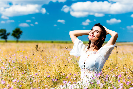 photo of the beautiful young woman in white dress sitting in the field in summer time