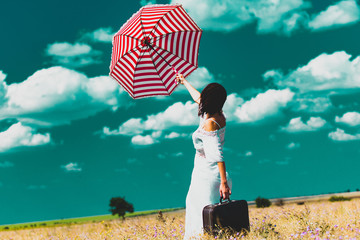 photo of the beautiful young woman with suitcase and umbrella in the field