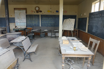 Dust gathering on the wooden desks and chairs in an abandoned elementary school.