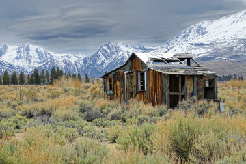Lonely wooden cabin decaying in the rugged wilderness under the snowy mountains.