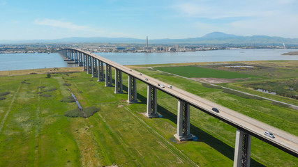 Fototapeta premium AERIAL Flying over vast meadow close to large concrete bridge crossing the river