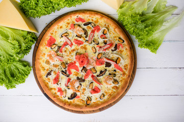 Delicious fresh Pizza with seefood (crabs and mussels) and cheese on the white wooden table surrounded by green salad and cheese